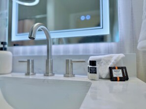 A bathroom with a modern sink, a mirror, and toiletries including a body cream and a facial bar. - The Colonial Mt. Lebanon by Luxe PGH (Pittsburgh)