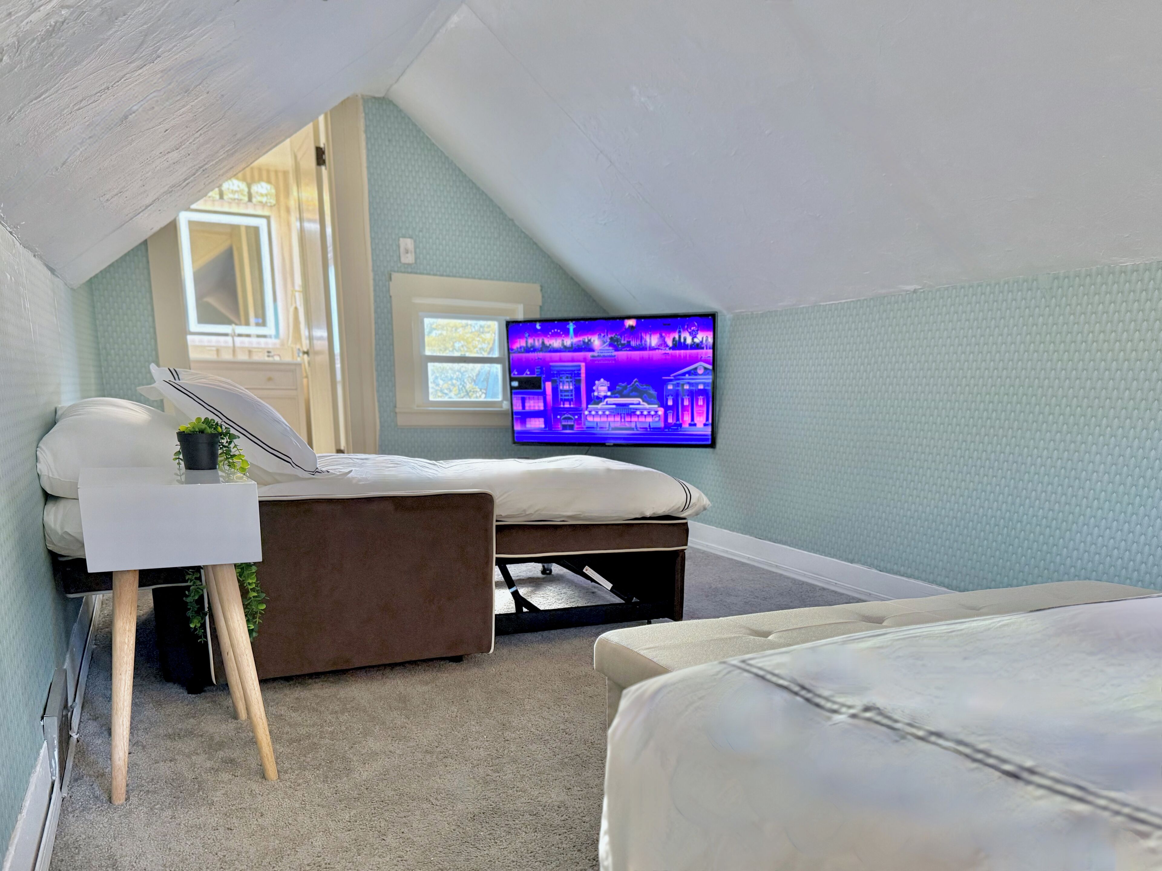 A bedroom with a bed, a small desk, a television, and a window.