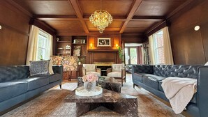 A spacious living room with dark wood paneling, a chandelier, leather sofas, a marble coffee table, and a fireplace. - The Colonial Mt. Lebanon by Luxe PGH (Pittsburgh)