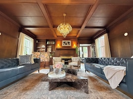 A spacious living room with dark wood paneling, a chandelier, leather sofas, a marble coffee table, and a fireplace.