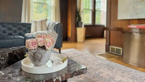 A living room with a marble coffee table, a vase of pink roses, a grey stone centerpiece, and a grey sofa. - The Colonial Mt. Lebanon by Luxe PGH (Pittsburgh)