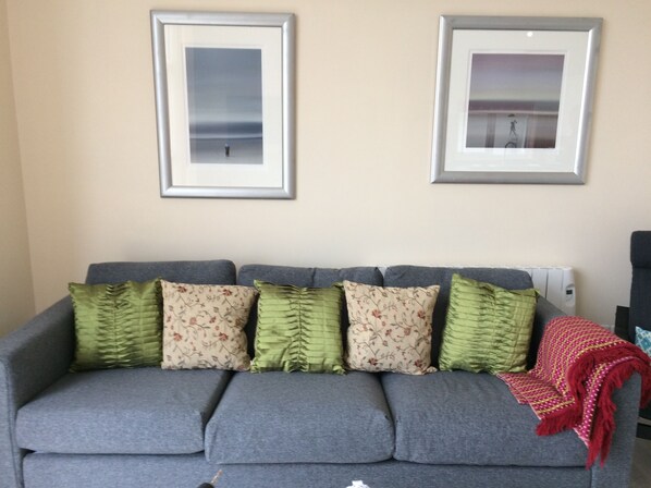 Ein graues Sofa mit mehreren Kissen, einer roten Decke und zwei gerahmten Bildern an der Wand.