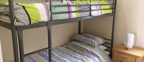 Una cama litera con ropa de cama a rayas y una mesita de noche de madera con un florero.