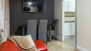 A modern living room with a red sofa, a TV mounted on a dark wall, and a dining area with two chairs and a table.