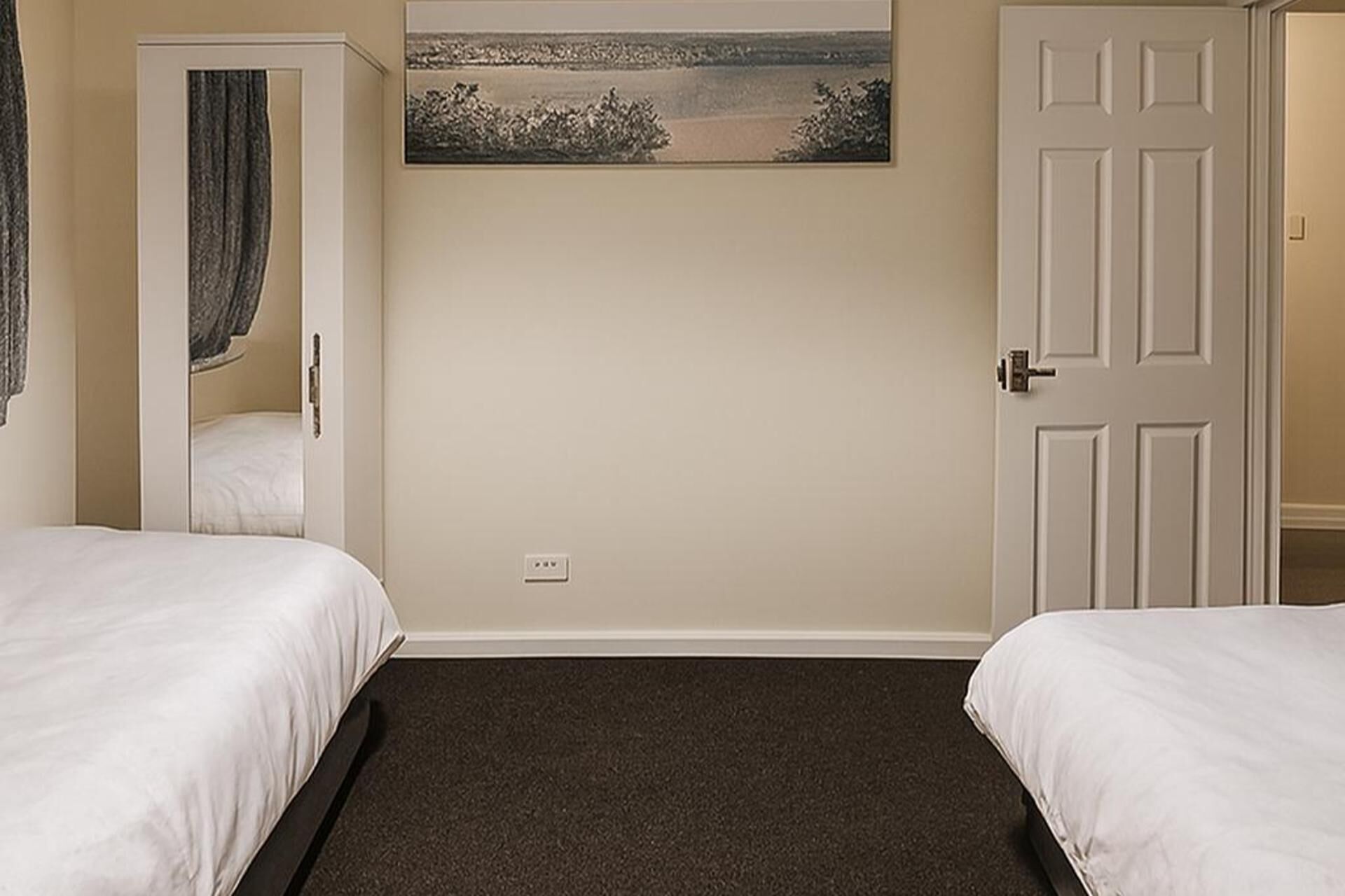 A room with two beds, a door, a painting, and a carpeted floor.