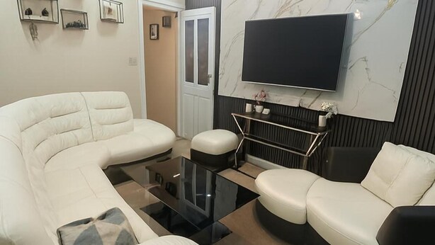 A modern living room with a sectional sofa, a coffee table, and a flat-screen TV mounted on the wall.