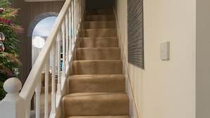A carpeted staircase with white balusters and a handrail, leading to an upper floor.