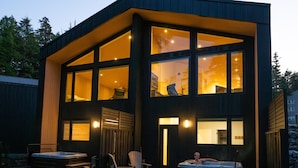 Une maison moderne à deux étages, dotée de grandes fenêtres, d’un jacuzzi et d’un espace salon extérieur.