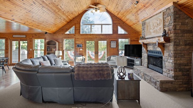 Interior acogedor de una cabaña de troncos con un amplio sofá modular en forma de L, una chimenea de piedra y un televisor.