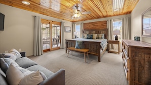 Una habitación acogedora con techo de madera, una cama con colcha escocesa, un sofá gris y un pequeño banco de madera.