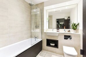 Un baño moderno con ducha de vidrio, una bañera blanca, un lavamanos con espejo y un inodoro.
