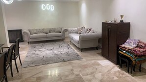 A modern living room with two sofas, a dining area with chairs, a marble floor, and a cabinet with folded blankets.