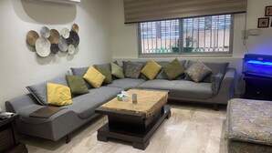 A modern living room with a grey sectional sofa, a wooden coffee table, and a patterned ottoman.
