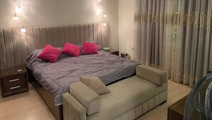 A bedroom with a bed, bedside tables, a bench, and a large window with curtains.