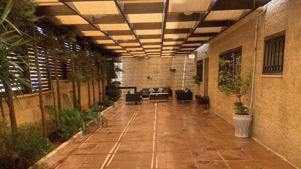 A covered outdoor area with tiled flooring, seating arrangements, and potted plants.