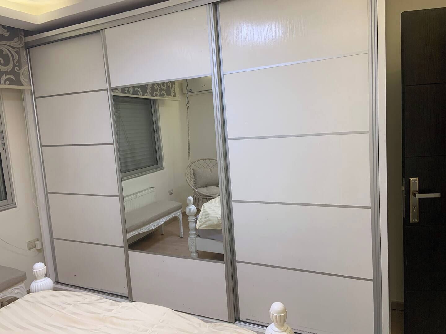 Quarto com um guarda-roupa deslizante espaçoso, uma cama com cabeceira branca e uma janela com persianas.