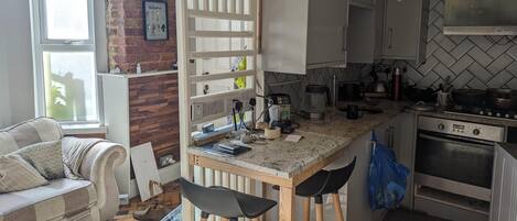 A kitchen with a brick wall, white cabinets, a coffee maker, and a stove.