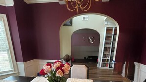 A room with a dark wooden floor, a white fur rug, a vase with flowers, and a chandelier.