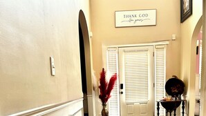A hallway with wooden flooring, white walls, and a door with a sign above it that reads "THANK GOD I'm outdoors."