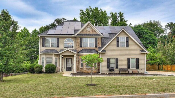 A two-story house with a front porch, solar panels, and a well-maintained lawn.