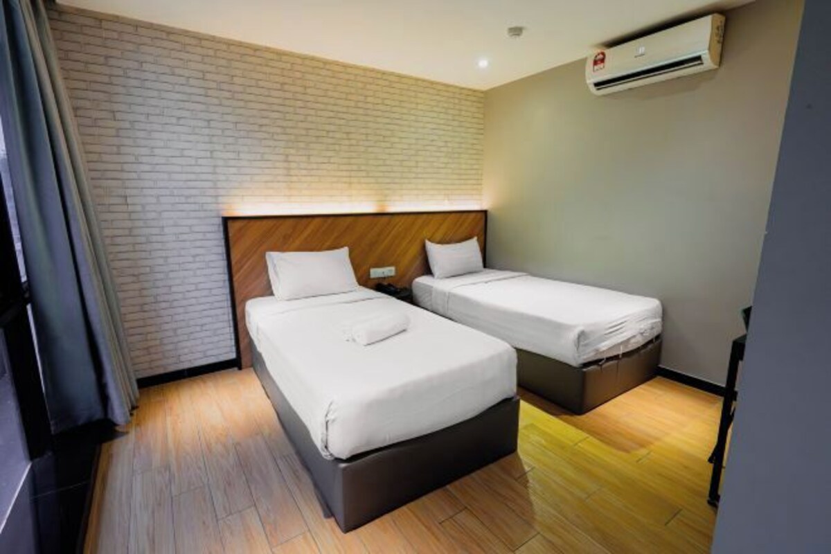 Habitación de hotel con dos camas, pared de ladrillo, unidad de aire acondicionado y piso de madera.