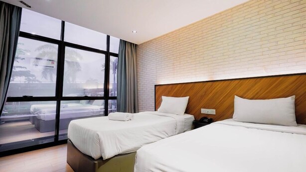 A hotel room with two beds, a brick wall, and a large window with a view of palm trees.