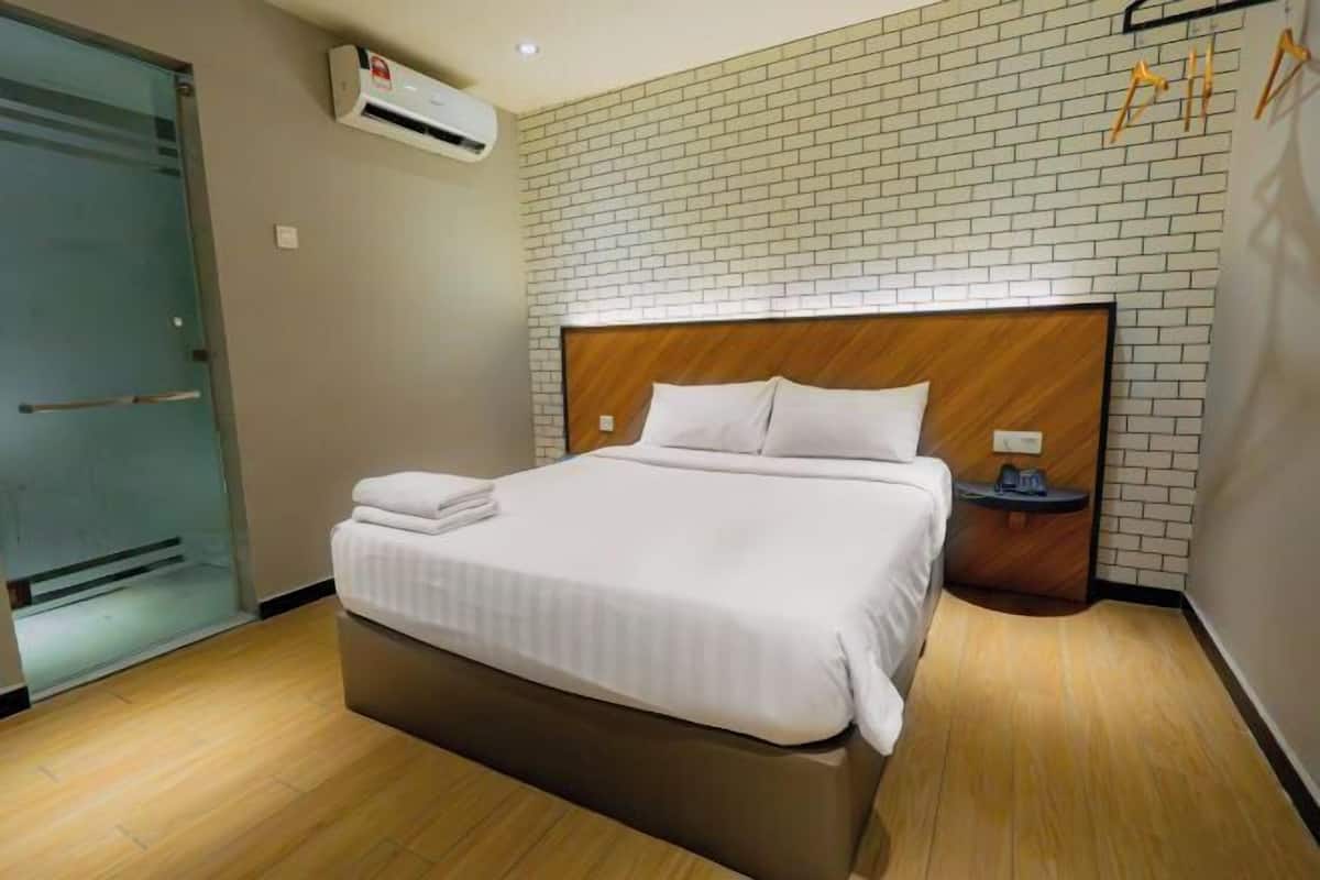 Hotellihuone, jossa on sänky, yöpöytä, seinään asennettu ilmastointilaite ja tiilikuviolla koristeltu seinä.