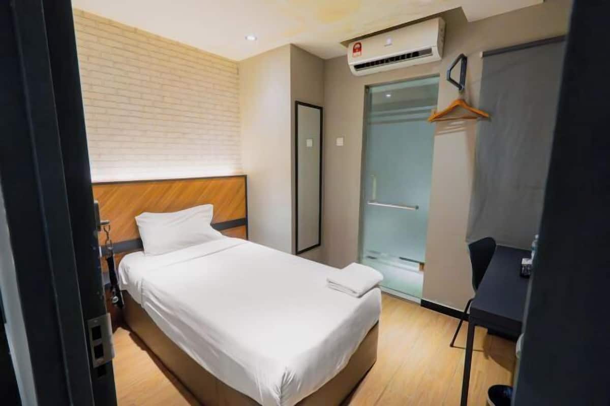 Hotellihuone, jossa on sänky, vaatekaappi, työpöytä ja ilmastointilaite.