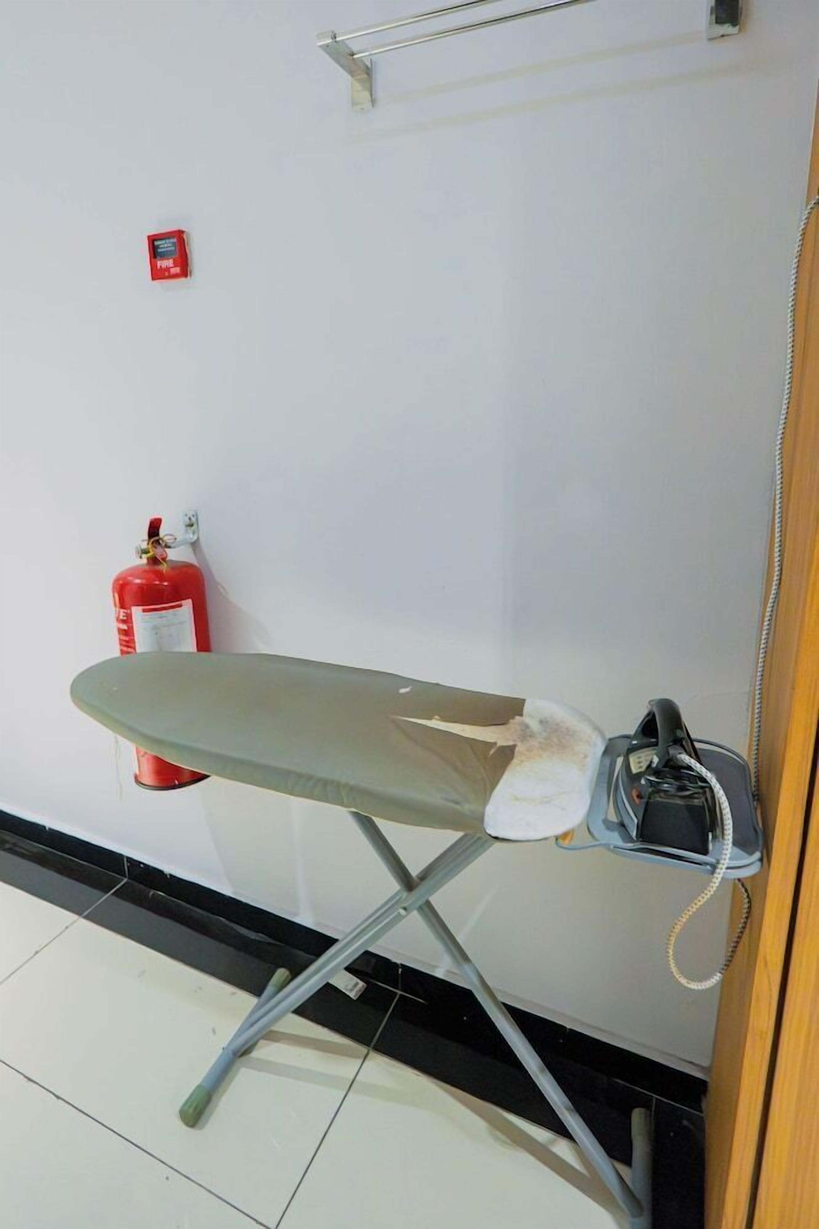 Ein Zimmer mit einem Klappbügelbrett, einem roten Feuerlöscher und einem an der Wand befestigten Telefon.