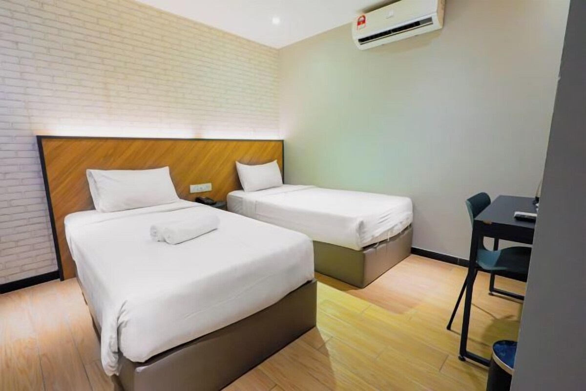A hotel room with two beds, a desk, and an air conditioning unit.