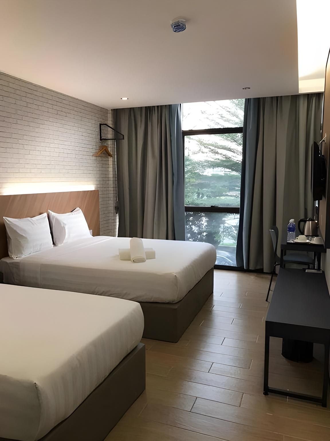 A hotel room with two beds, a desk, and a large window with curtains.