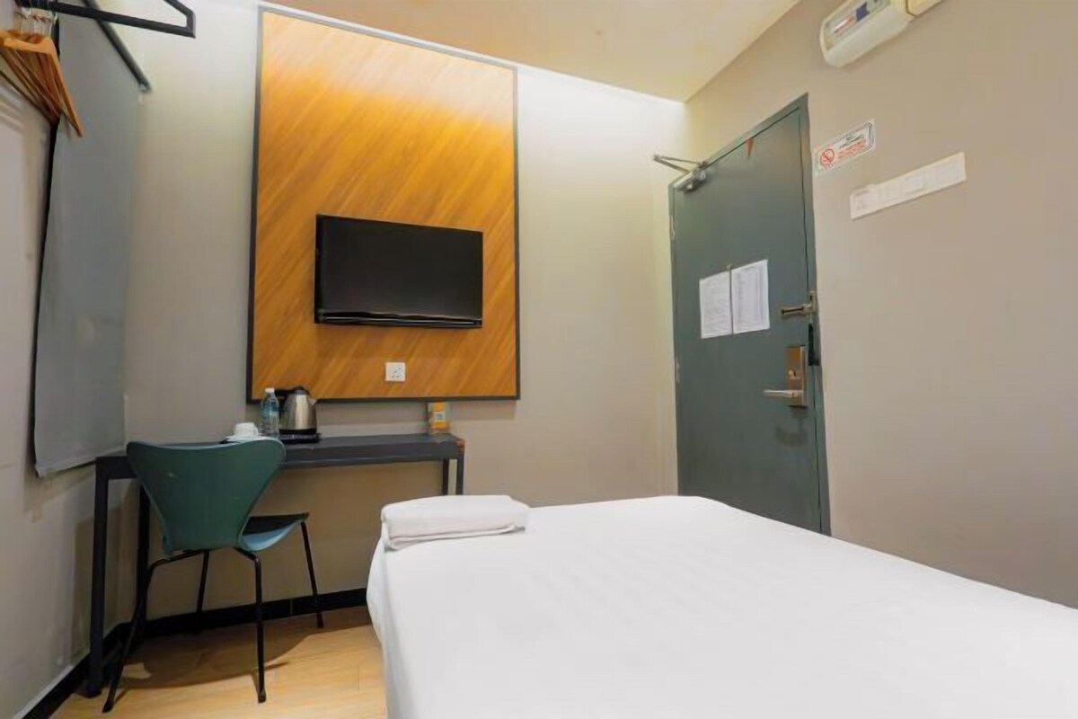 Una habitación de hotel con una cama, un escritorio con una silla, un televisor en la pared y una puerta con un cartel.