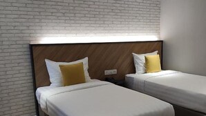 Two single beds with wooden headboards, white bedding, and yellow pillows in a room with a brick-patterned wall.