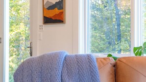 A room with a brown leather sofa, a framed artwork on the wall, and a window with a view of trees. - Spacious 6BR VT Retreat w/Sauna & Golf Simulator Near Stowe, Smuggs & Jay Peak (Johnson)