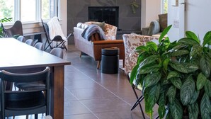 A modern living room with a fireplace, a dining area with a table and chairs, and a large potted plant. - Spacious 6BR VT Retreat w/Sauna & Golf Simulator Near Stowe, Smuggs & Jay Peak (Johnson)