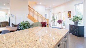 A modern kitchen with granite countertops, a wooden staircase, and a dining area with a table and chairs. - Spacious 6BR VT Retreat w/Sauna & Golf Simulator Near Stowe, Smuggs & Jay Peak (Johnson)