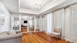 A spacious room with a wooden floor, a grey sofa, a chair, and a large mirror reflecting the room. - The Driftwood on Magazine (New Orleans)