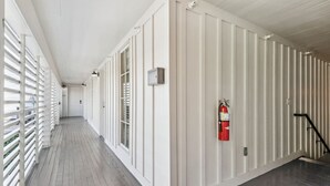 A corridor with white paneling, a fire extinguisher, and a staircase. - The Driftwood on Magazine (New Orleans)