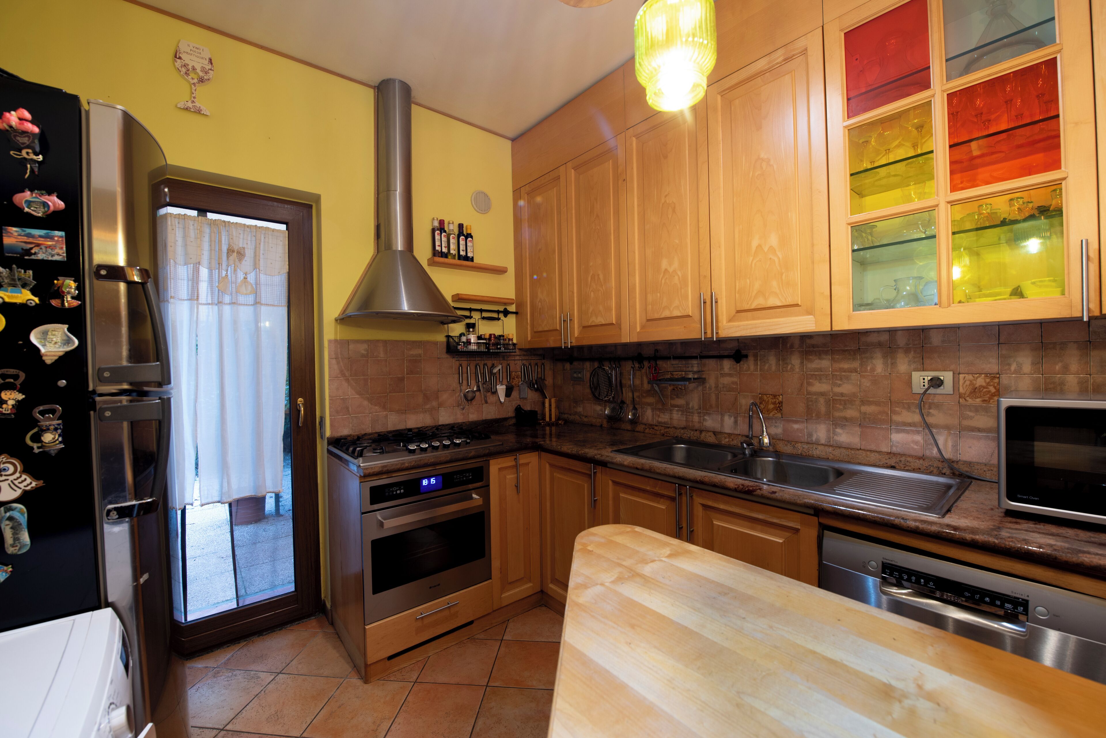Une cuisine avec des meubles en bois, des appareils électroménagers en acier inoxydable et une fenêtre avec des rideaux.