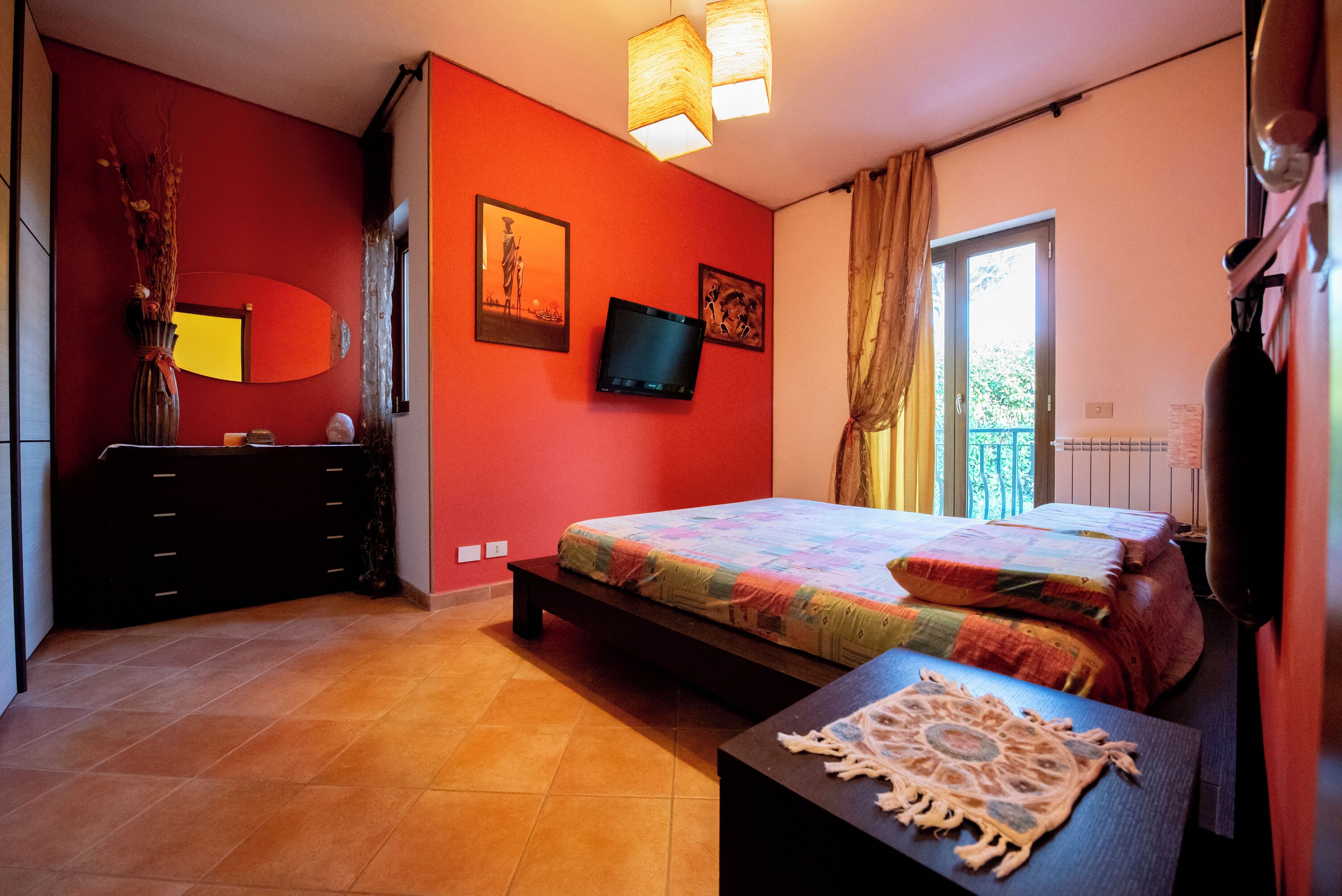 Une chambre à coucher avec un lit, une télévision, une commode et une fenêtre avec des rideaux.