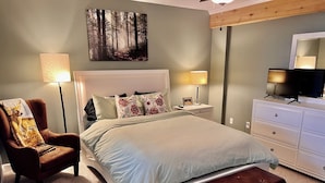 Une chambre à coucher comprenant un lit, une chaise, un banc, une commode, un téléviseur et un tableau accroché au mur.