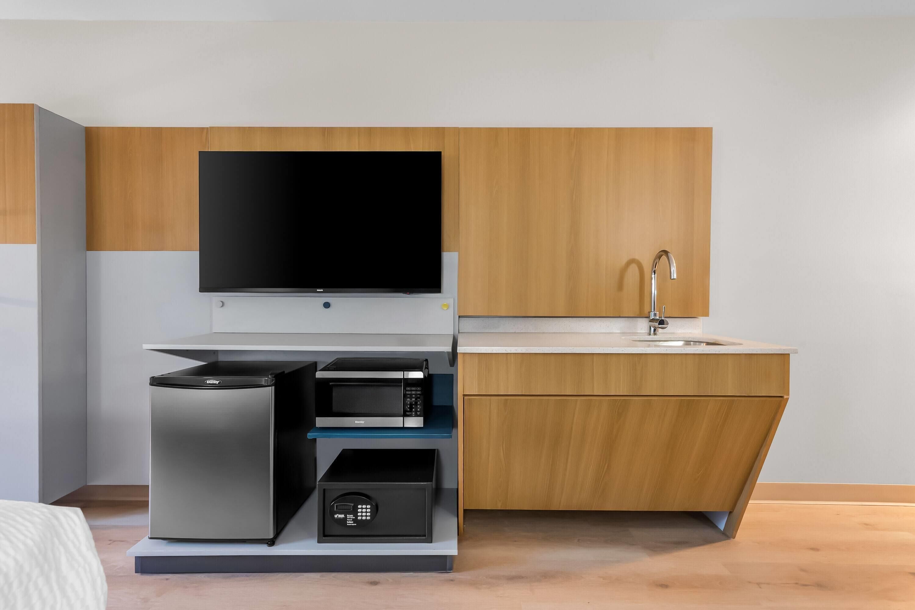 Cocina compacta con televisor de pantalla plana, microondas y pileta integrada.