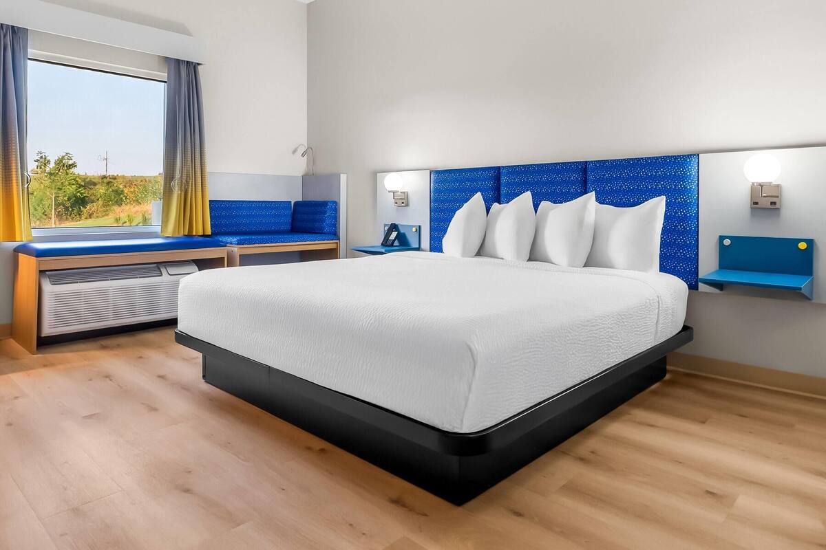 Quarto de hotel moderno com uma cama grande, uma escrivaninha e vista para o exterior.