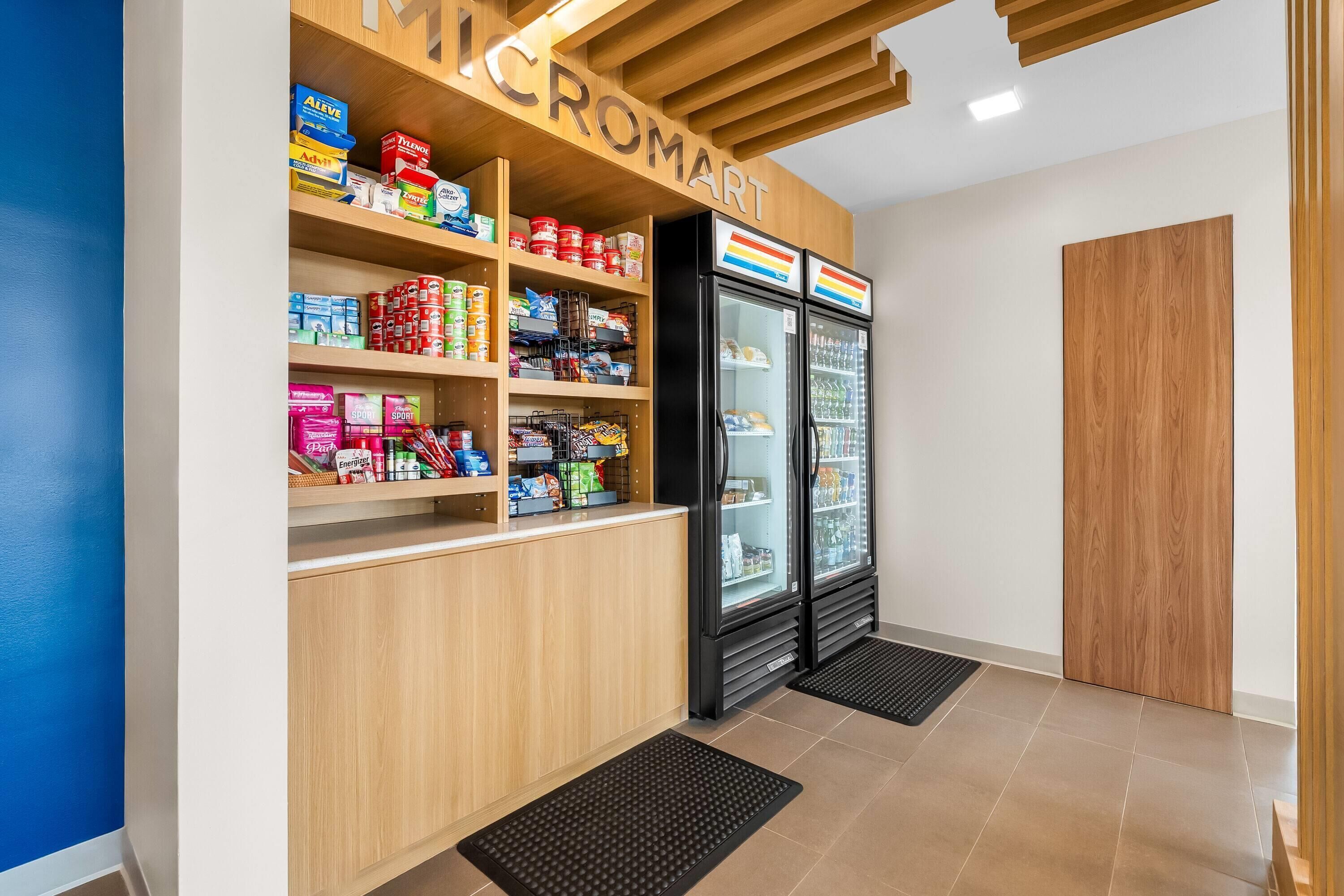 L’intérieur d’une épicerie, avec des étagères remplies de divers produits, un présentoir réfrigéré et un comptoir en bois.