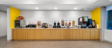 A modern kitchen area with a wooden counter, various appliances, and a yellow accent wall.