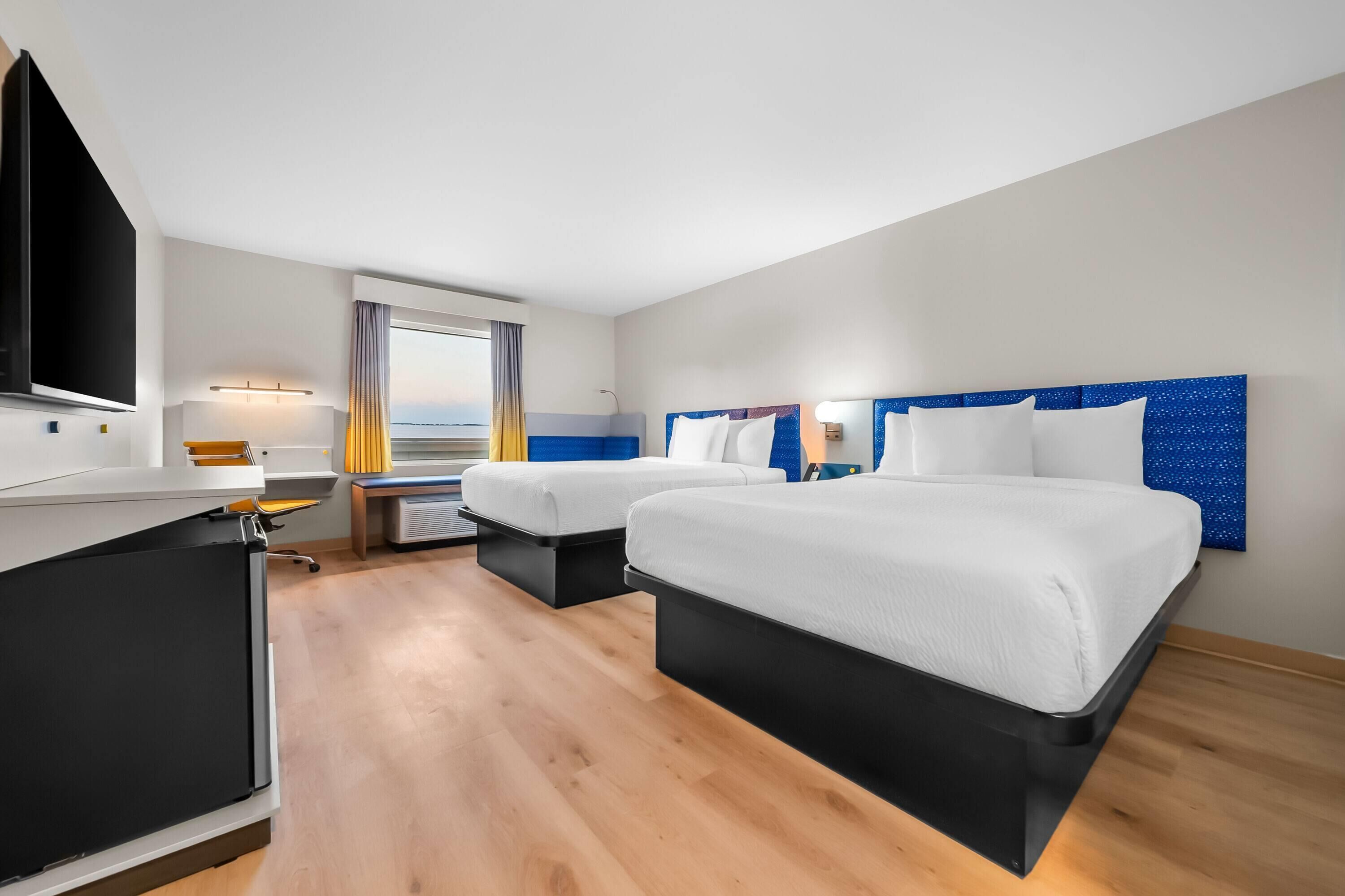 Habitación de hotel con dos camas, un escritorio, un televisor y una ventana con cortinas.