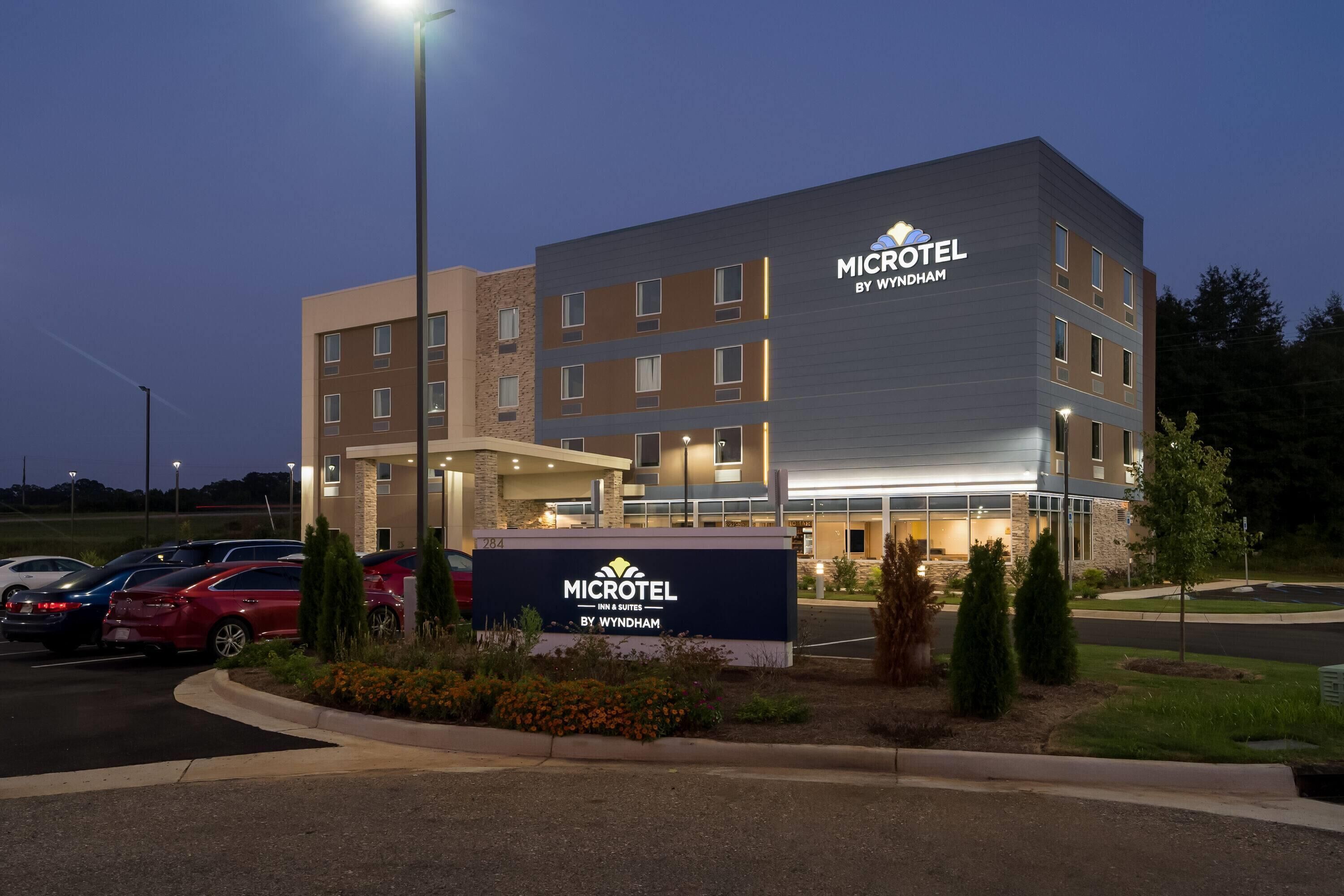 A Microtel Inn & Suites building with a parking lot and a landscaped area with shrubs and flowers.