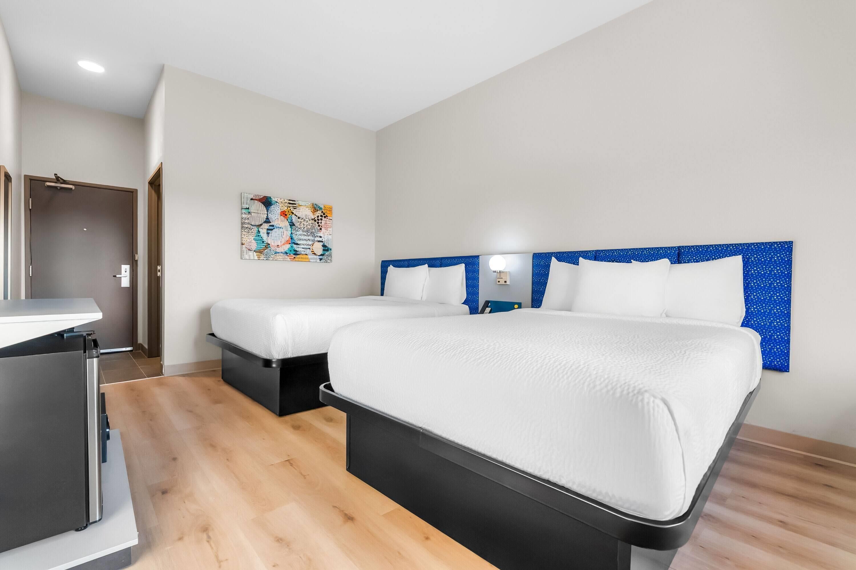 Habitación de hotel con dos camas, un escritorio y una obra de arte colgada en la pared.