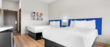Habitación de hotel con dos camas, un escritorio y una obra de arte colgada en la pared.