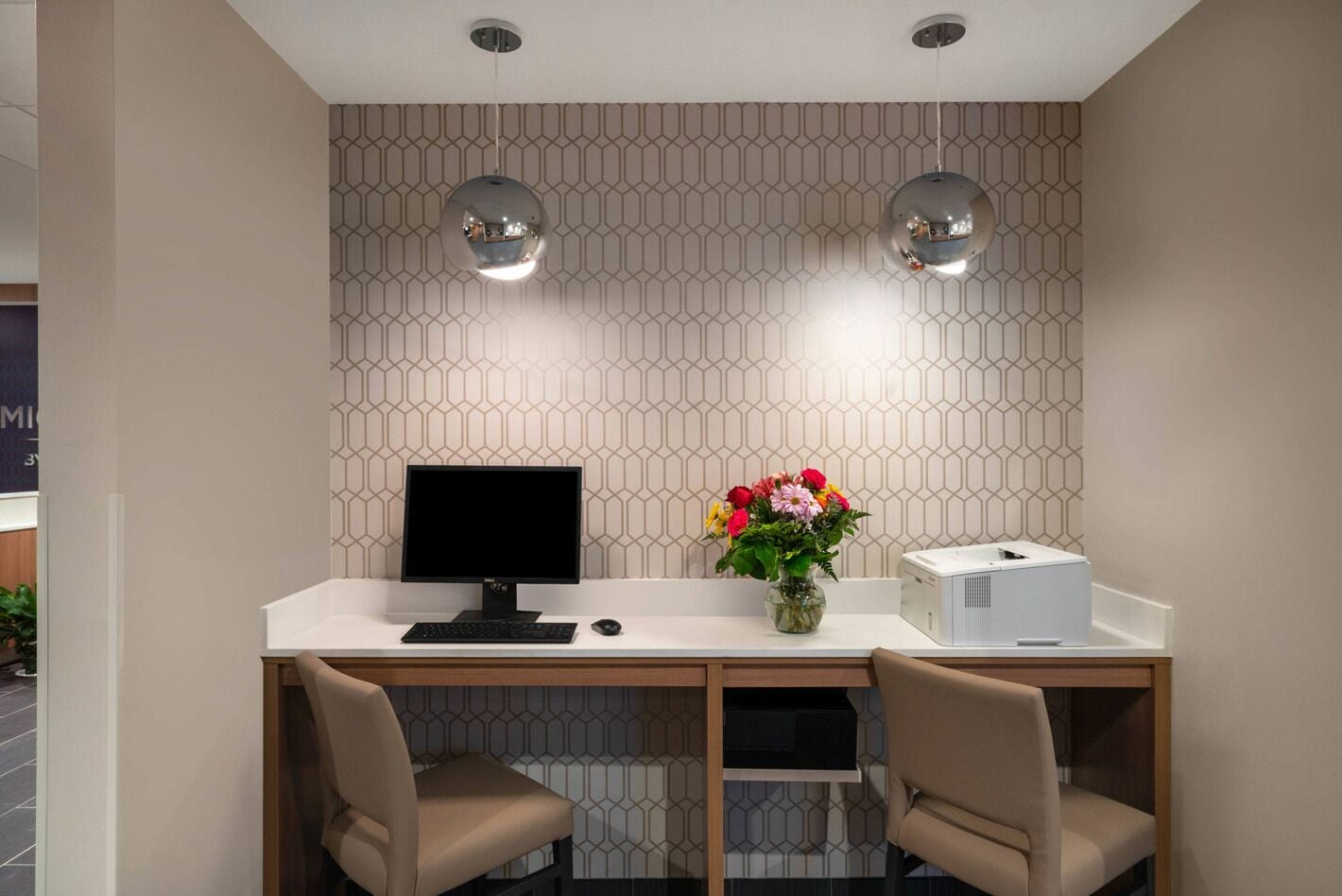 Un bureau moderne, équipé d’un ordinateur, d’un vase de fleurs et d’une imprimante.